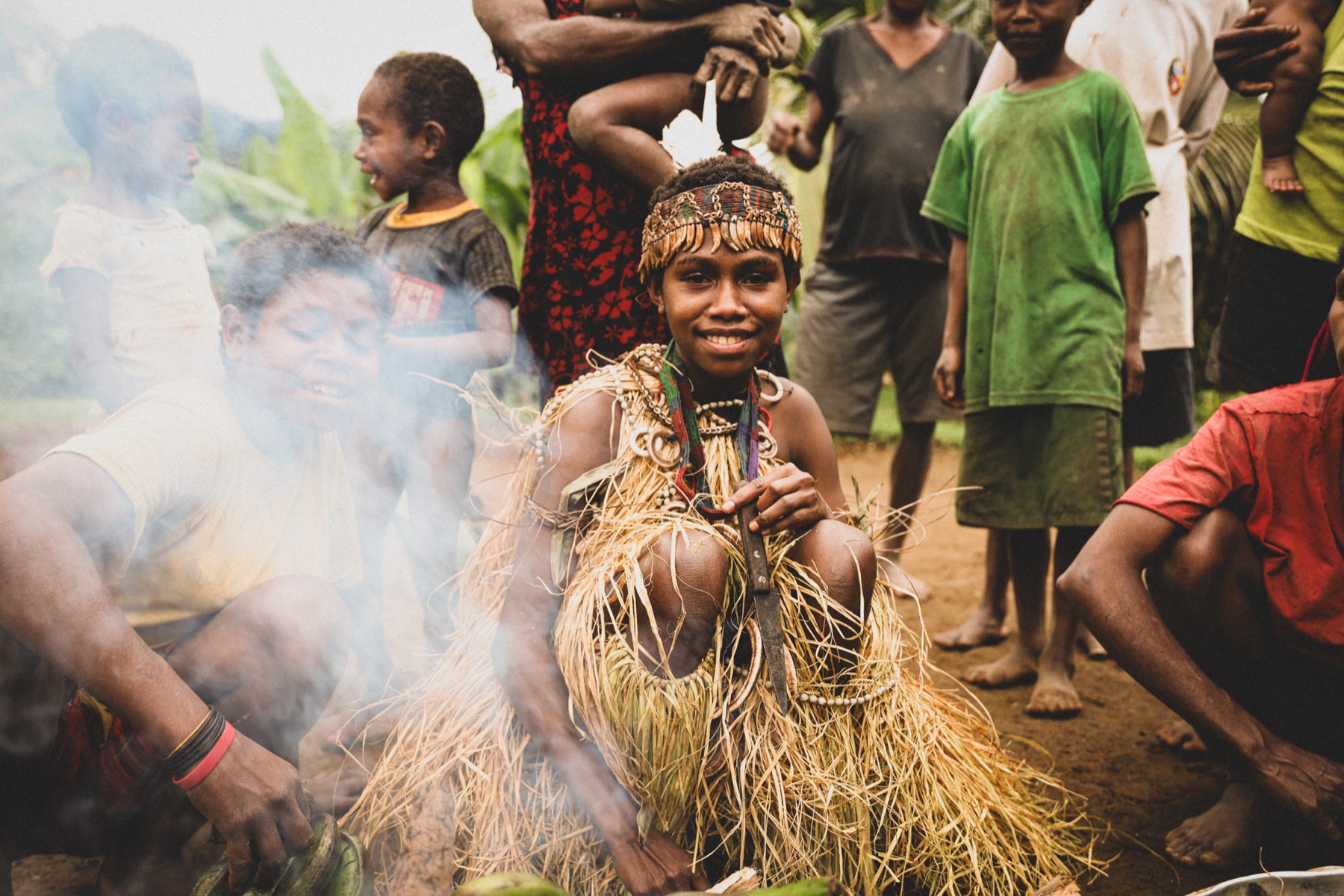 A smiling young person wearing traditional adornments at a community gathering.