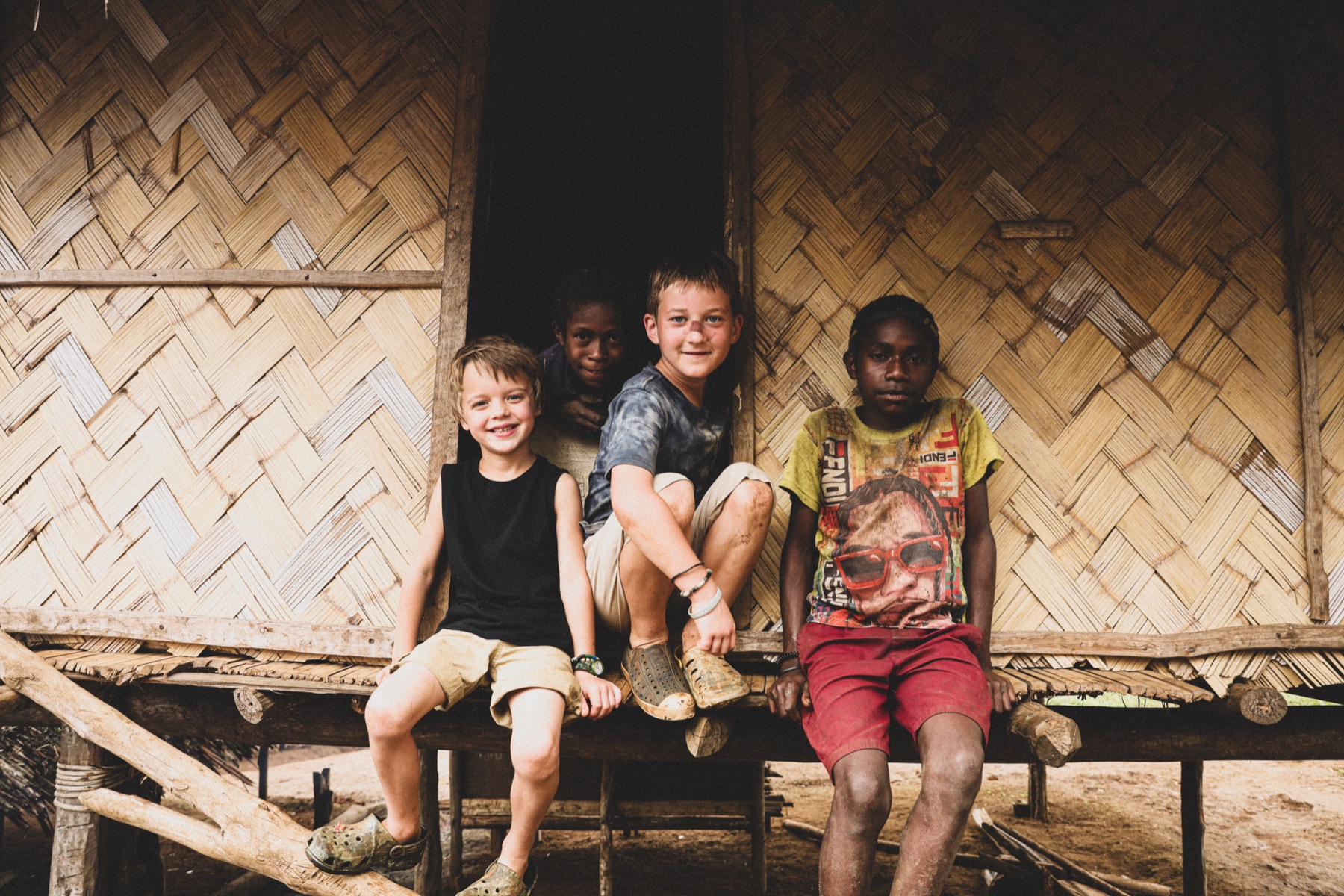 Children sitting together in the doorway of a woven-wall home.